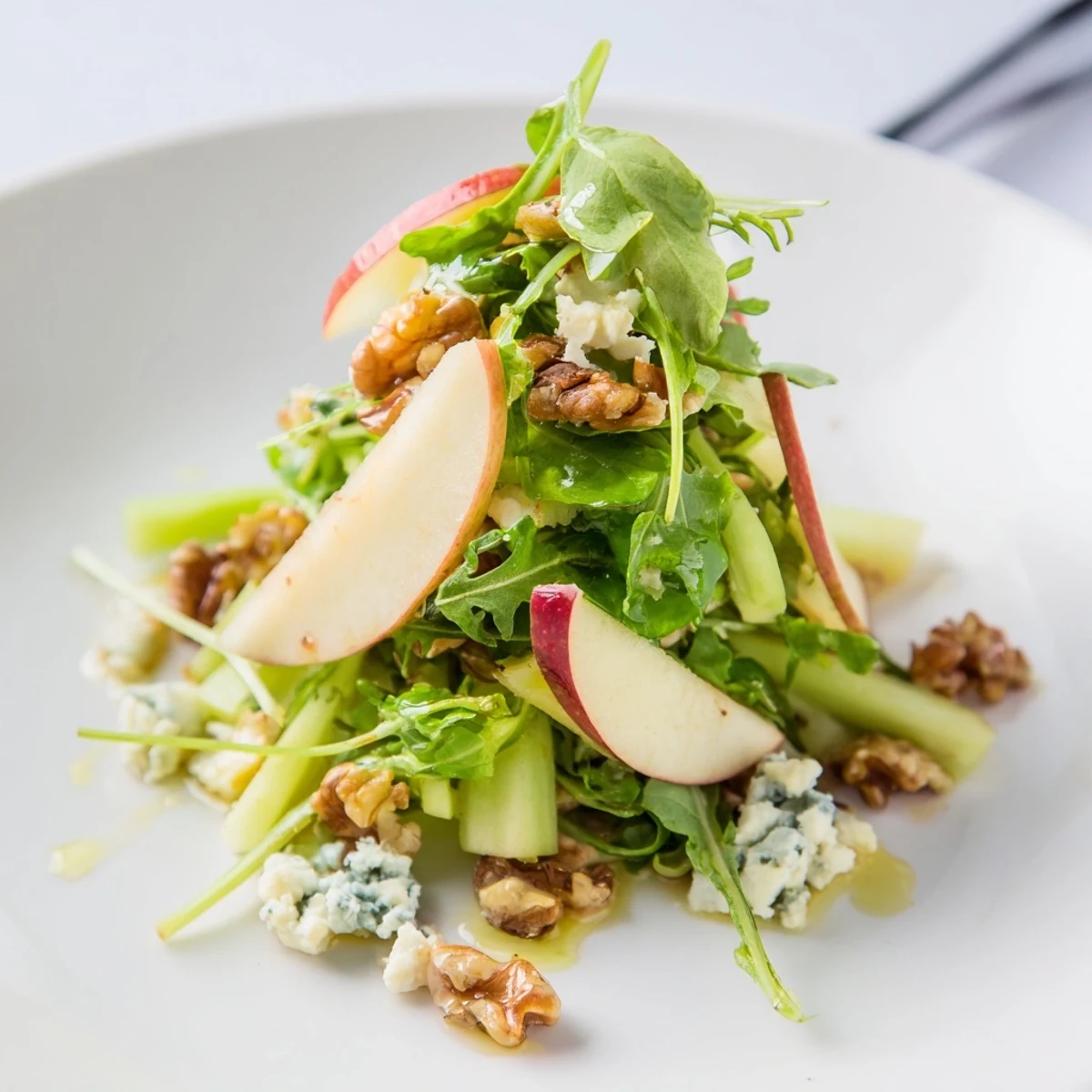 A vibrant bowl of Apple and Walnut Salad featuring crisp celery, feta crumbles, and a drizzle of zesty apple cider dressing.  