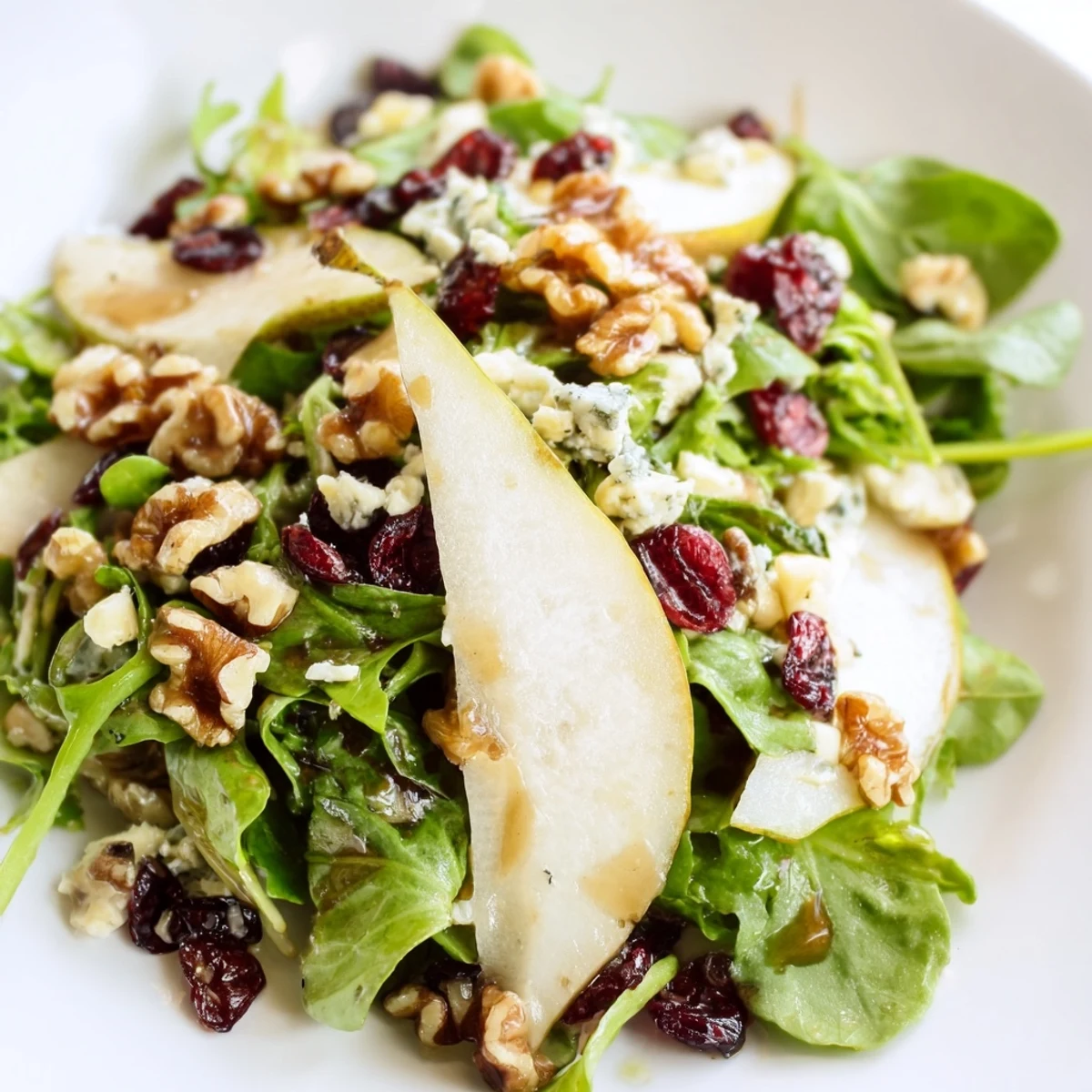 Sliced ripe pears and crumbled Gorgonzola cheese top mixed greens, toasted walnuts, and cranberries on a plate, drizzled with honey-balsamic vinaigrette.  