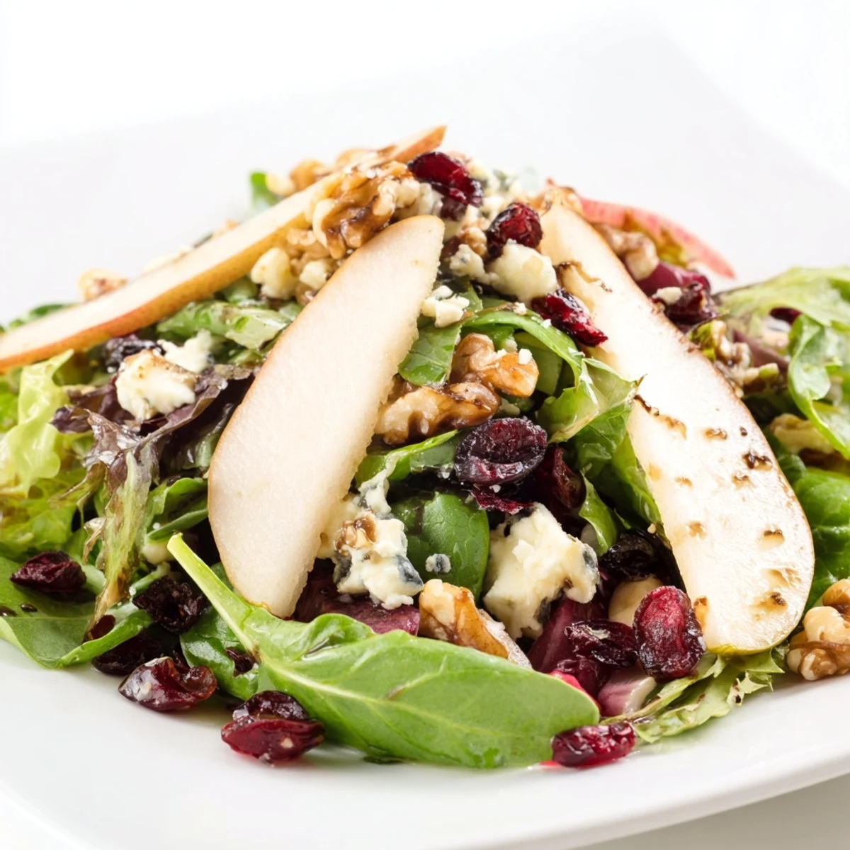 Close-up of Pear Gorgonzola Salad ingredients: sweet pear slices, tangy Gorgonzola, toasted walnuts, and dried cranberries tossed with mixed greens.