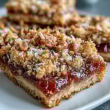 Golden-baked Guava Jam Bars on a rustic wooden board, cut to reveal layers of buttery oat crust, sweet guava jam, and chunky macadamia topping.