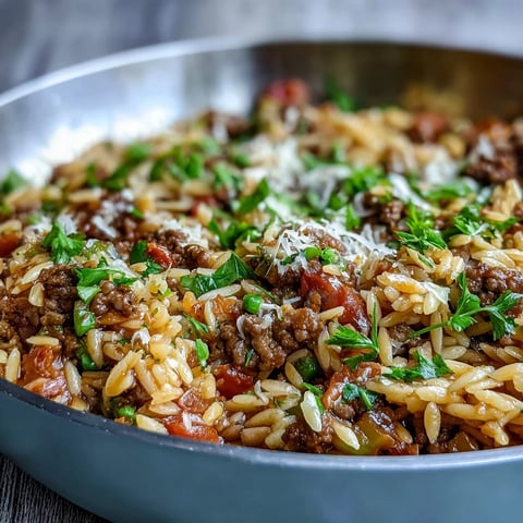Steaming Comforting Ground Beef Orzo Dinner in a cast iron skillet, topped with fresh parsley and grated Parmesan, perfect for weeknight family dinners.
