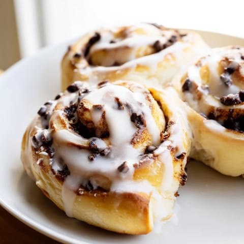 Golden-brown Nutella Chocolate Chip Rolls fresh from the oven, drizzled with sweet glaze on a rustic wooden table.