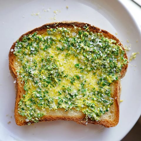 Golden Herb Butter Toast sits atop a rustic cutting board, with fresh parsley and chives scattered nearby.  