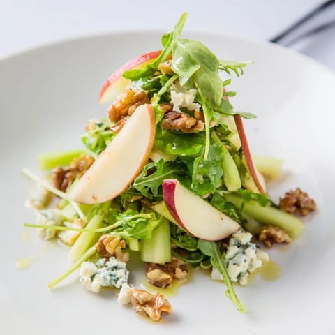 A vibrant bowl of Apple and Walnut Salad featuring crisp celery, feta crumbles, and a drizzle of zesty apple cider dressing.  