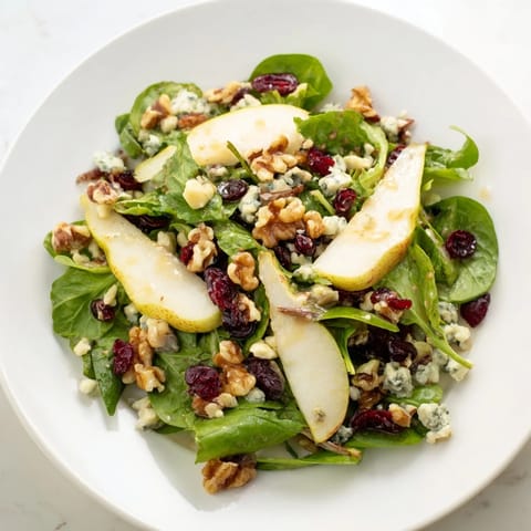 A vibrant bowl of Pear Gorgonzola Salad with crisp greens, juicy pears, blue cheese crumbles, and walnuts beside a small dressing pitcher.  
