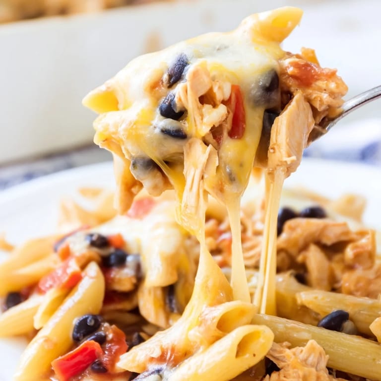 A close-up of creamy Chicken Enchilada Pasta in a serving dish, garnished with fresh cilantro and diced avocado for a fresh contrast.
