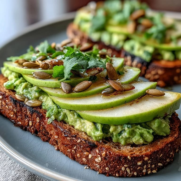 Creamy mashed avocado, crisp green apple slices, and toasted pumpkin seeds create a vibrant, healthy breakfast toast.