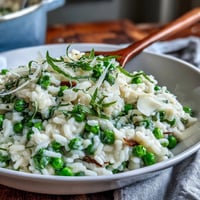 A bowl of creamy spring pea risotto garnished with fresh mint and grated Parmesan, perfect for a vegetarian spring dinner.  